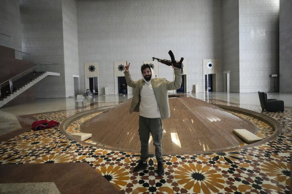 ‘The Fall of Damascus’ a Historic Moment for Syria 1 A man holds an AK-47 and flashes the victory sign as he poses for a photo in a hall of Syrian President Bashar Assad's presidential palace in Damascus, Syria, on December 8, 2024. | Photo Credit: AP
